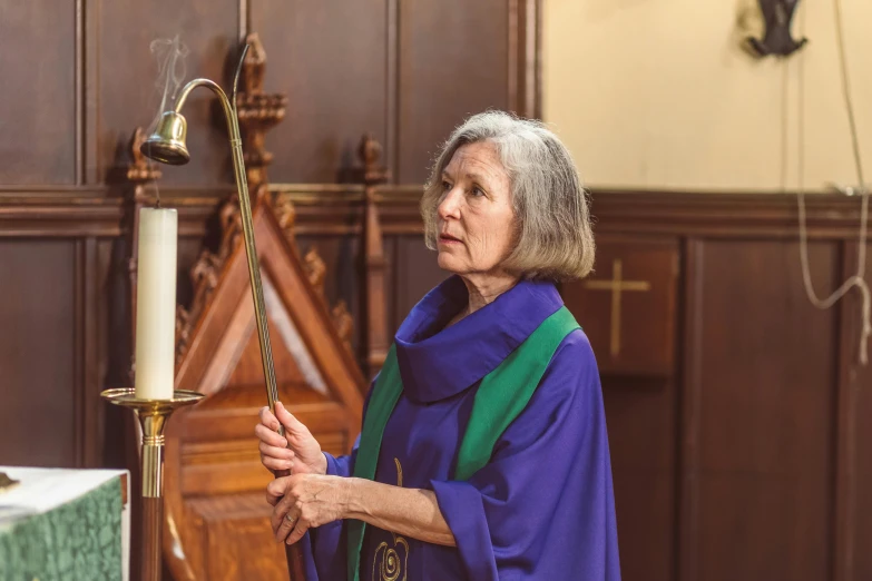 a woman standing next to a candle in a church, purple robes, older woman, vibrating, a green