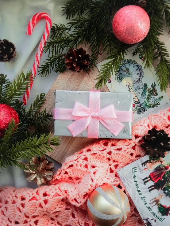 a table topped with christmas decorations and a book, by Julia Pishtar, pexels contest winner, happening, pink concrete, holding a bow, anna nikonova aka newmilky, gif