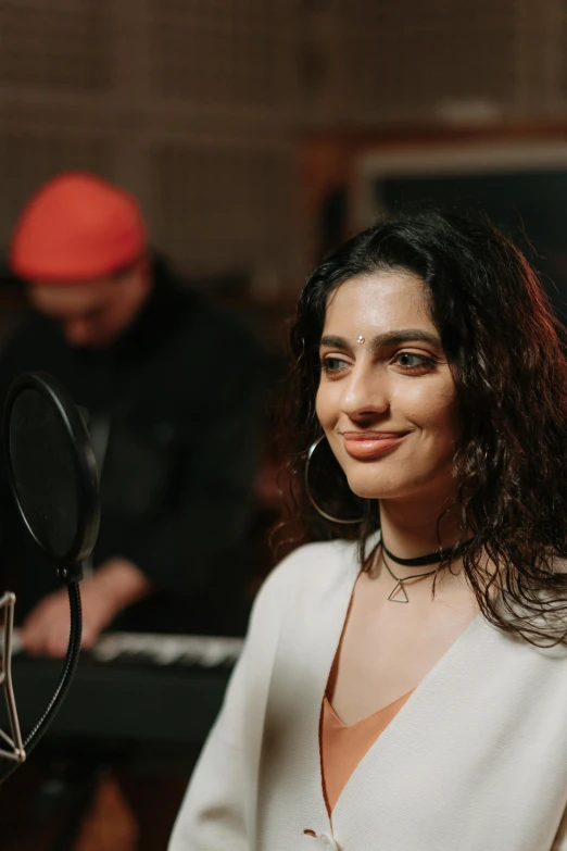 a woman sitting in front of a microphone, an album cover, trending on pexels, serial art, young middle eastern woman, lovingly looking at camera, behind the scenes photo, foreground