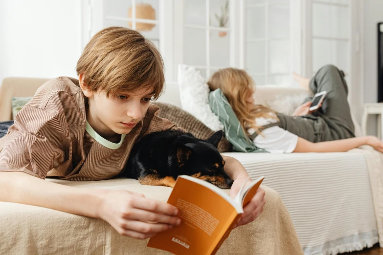 a young boy laying on a couch reading a book, a cartoon, pexels contest winner, boy with cat ears and tail, teenage boy, with small cat on lap, subject: dog