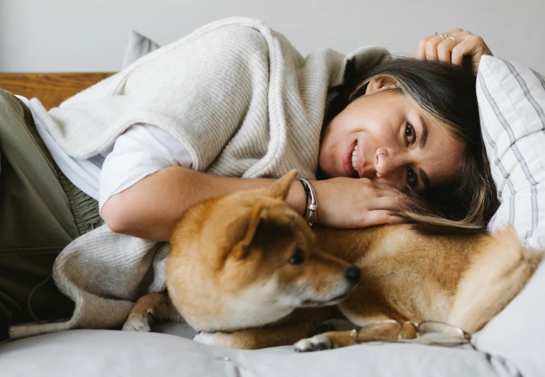 a woman laying on top of a bed next to a dog, trending on pexels, cuddling her gremlings, shibu inu, profile image, australian