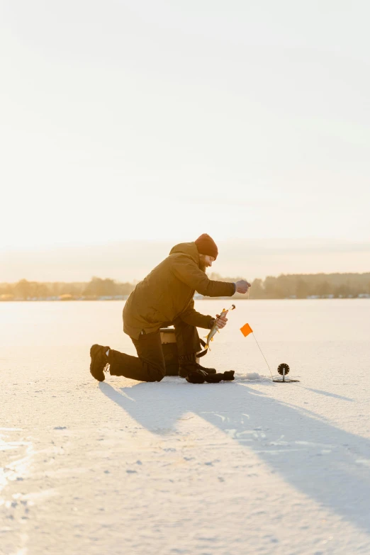 a man kneeling on top of a snow covered field, fishing, launch test, during golden hour, mechanics