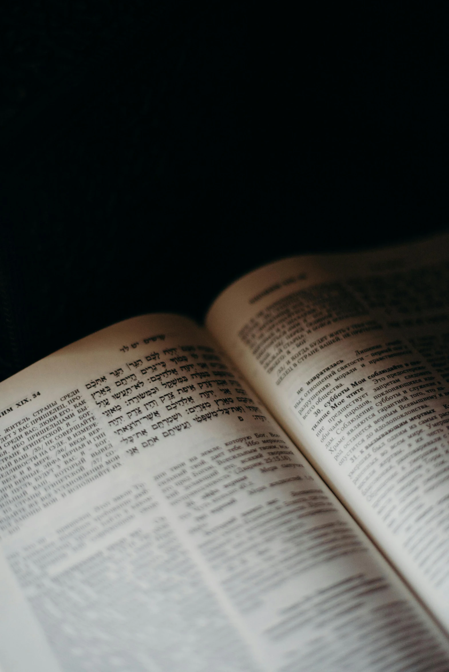 an open book sitting on top of a table, in front of a black background, hebrew, over-the-shoulder shot, holy