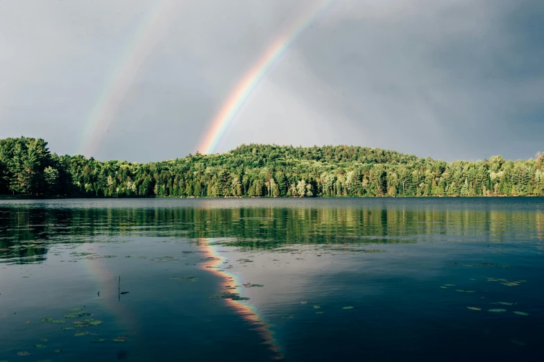 a large body of water with a rainbow in the sky, a photo, by Jaakko Mattila, unsplash contest winner, hudson river school, build in a forest near of a lake, grey skies with two rainbows, quebec, shot on kodak ektar