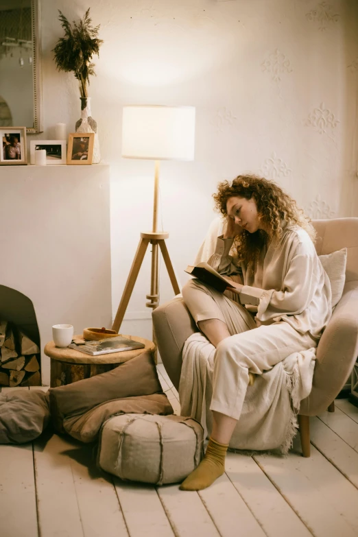 a woman sitting in a chair reading a book, trending on pexels, happening, wearing white pajamas, emerging from her lamp, brown, full length shot