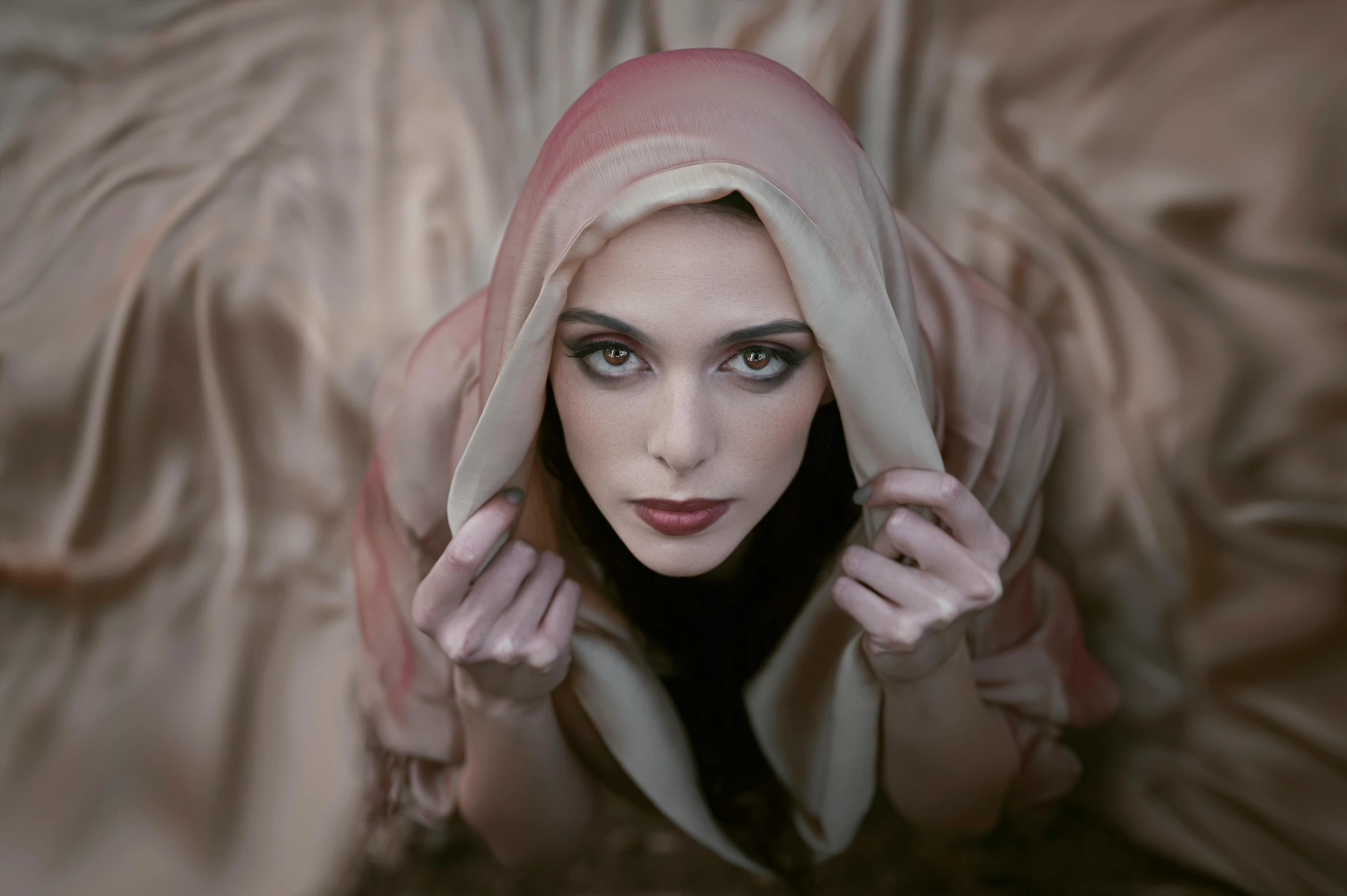 a woman laying on top of a bed covered in a blanket, a portrait, inspired by Brooke Shaden, pexels contest winner, renaissance, wearing pointed hoods, looking into camera, white and pink cloth, clothed in silk