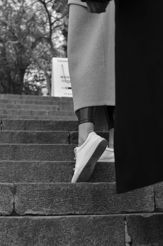 a black and white photo of a woman walking up a flight of stairs, inspired by Louis Stettner, unsplash, wearing white sneakers, walk in a funeral procession, wearing jacket and skirt, gum rubber outsole