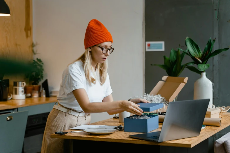 a woman sitting at a table typing on a typewriter, a cartoon, trending on pexels, baggy clothing and hat, delivering parsel box, in a workshop, professional product photo