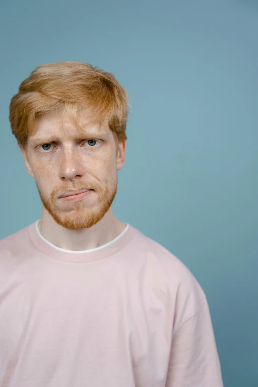 a man standing in front of a blue background, an album cover, by Lasar Segall, trending on pexels, hyperrealism, ginger hair with freckles, sad exasperated expression, 15081959 21121991 01012000 4k, justin roiland