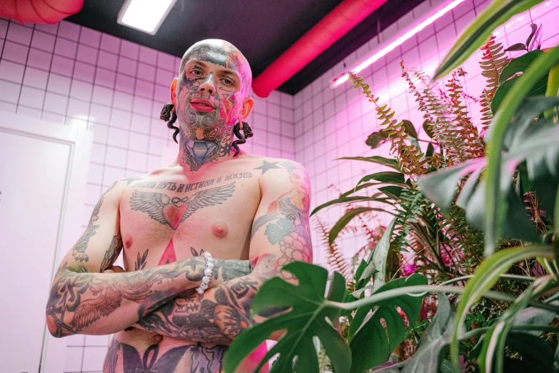 a man with tattoos standing next to a potted plant, inspired by Seb McKinnon, pexels contest winner, brightly lit pink room, with facial tattoo, plastic skin, ariel perez