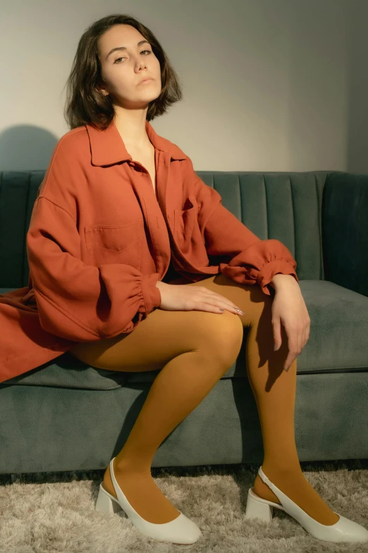 a woman sitting on top of a green couch, inspired by Balthus, trending on pexels, tights, orange jacket, ocher, lookbook