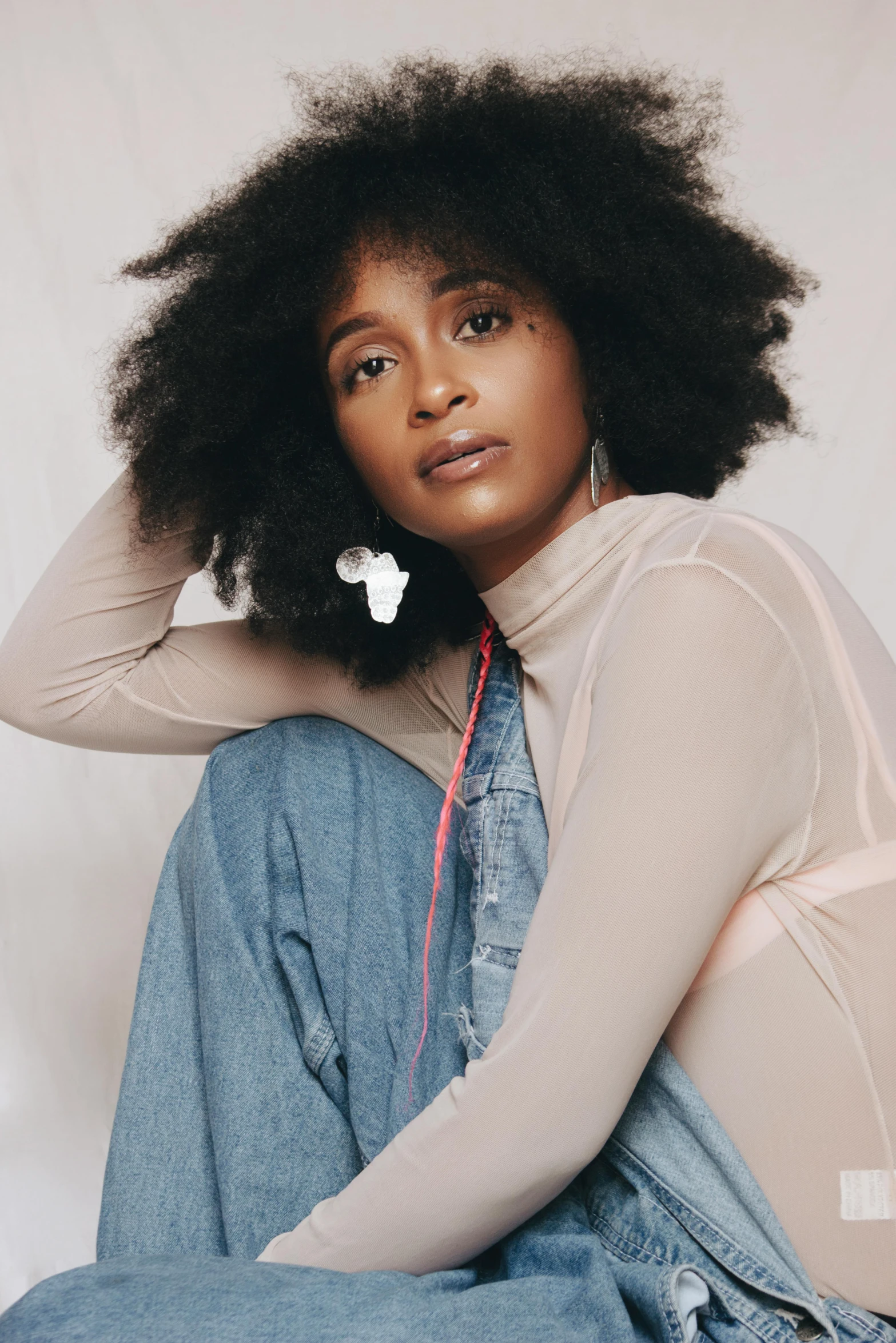 a woman sitting on the ground with a cell phone in her hand, an album cover, by Lily Delissa Joseph, trending on pexels, renaissance, natural hair, earbuds jewelry, wearing turtleneck, delicate soft hazy lighting