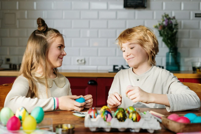 a couple of kids that are sitting at a table, pexels contest winner, holding easter eggs, profile image, board games on a table, promotional image