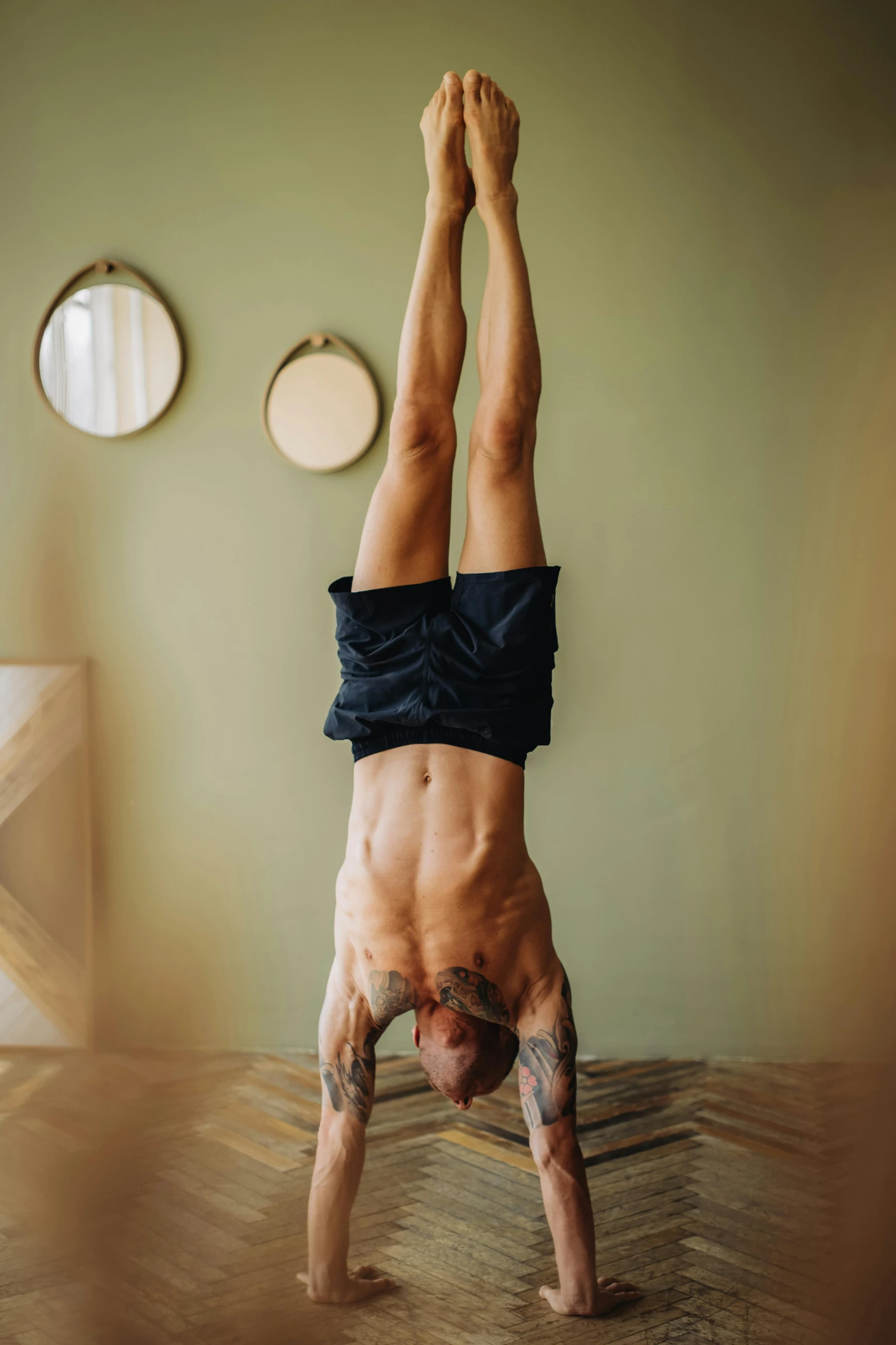 a man doing a handstand in a room, a tattoo, belly button showing, lgbtq, athletic body build, top down