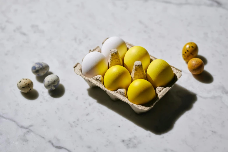 a carton filled with eggs sitting on top of a table, a still life, inspired by Sarah Lucas, unsplash, white and yellow scheme, hand grenades, all marble, miniature product photo