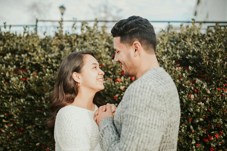 a man and woman standing next to each other in front of bushes, pexels contest winner, happening, dimples, background image, romantic, holiday season