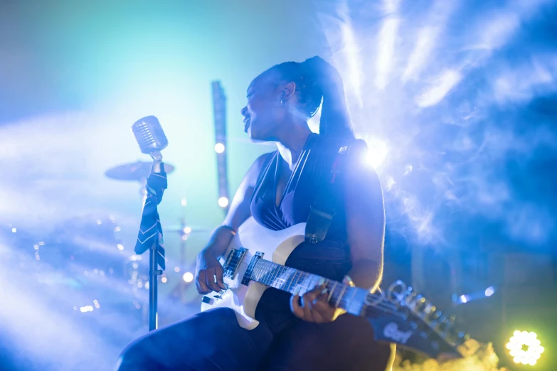 a woman playing a guitar in front of a microphone, pexels contest winner, happening, dramatic white and blue lighting, avatar image, maria borges, vibrant atmosphere