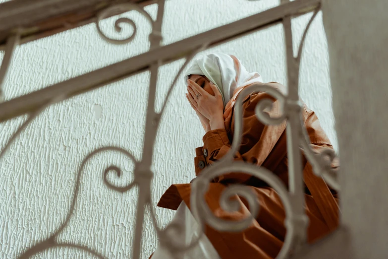 a close up of a person on a cell phone, a picture, inspired by Elsa Bleda, pexels contest winner, hurufiyya, hijab, distraught, standing astride a gate, brown clothes