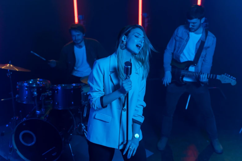 a group of people standing next to each other on a stage, an album cover, pexels, neon operator margot robbie, performing a music video, blue mood, indoor scene