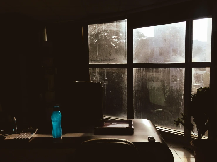 a laptop computer sitting on top of a desk in front of a window, inspired by Elsa Bleda, realism, rainy; 90's photograph, snapchat photo, sitting in dean's office, vibrant but dreary blue