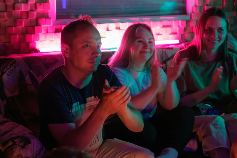 a group of people sitting on top of a couch, pink and blue lighting, parents watching, colourful lighting, excited russians