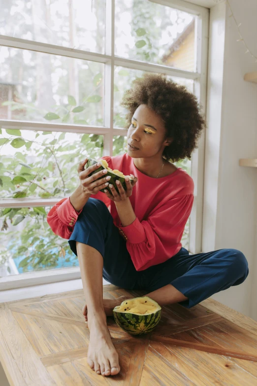 a woman sitting on a table eating a sandwich, by Lily Delissa Joseph, pexels, renaissance, holding an avocado in his hand, looking out window, wearing yellow croptop, bowl filled with food