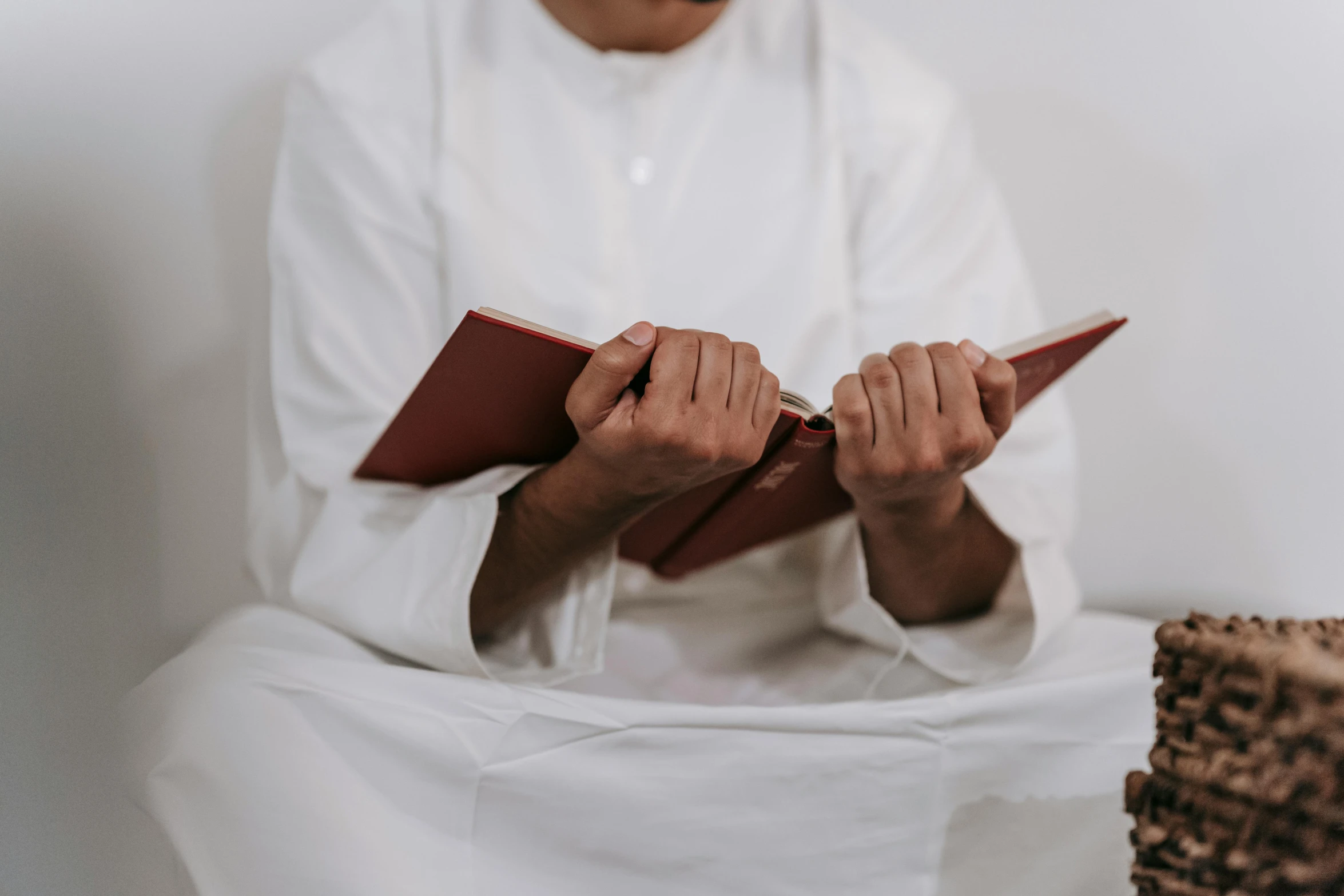 a man reading a book in front of a cake, inspired by Abdur Rahman Chughtai, pexels contest winner, hurufiyya, wearing white silk robe, closed hands, sitting on edge of bed, red brown and white color scheme