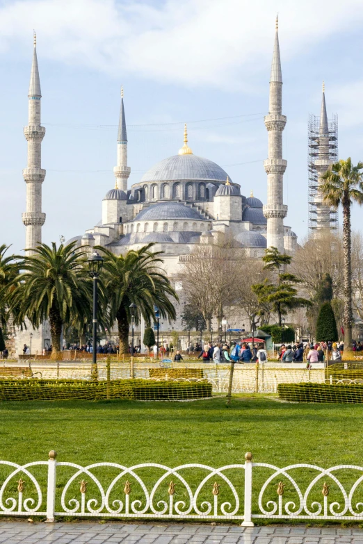 a man sitting on a bench in front of a building, inspired by Altoon Sultan, hurufiyya, tall stone spires, people resting on the grass, formal gardens, blue sky