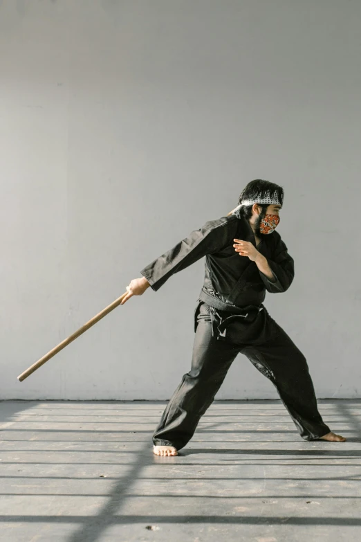 a man standing on top of a wooden floor holding a stick, inspired by Kanō Hōgai, unsplash, shin hanga, preparing to fight, high-quality photo, black, tai costume