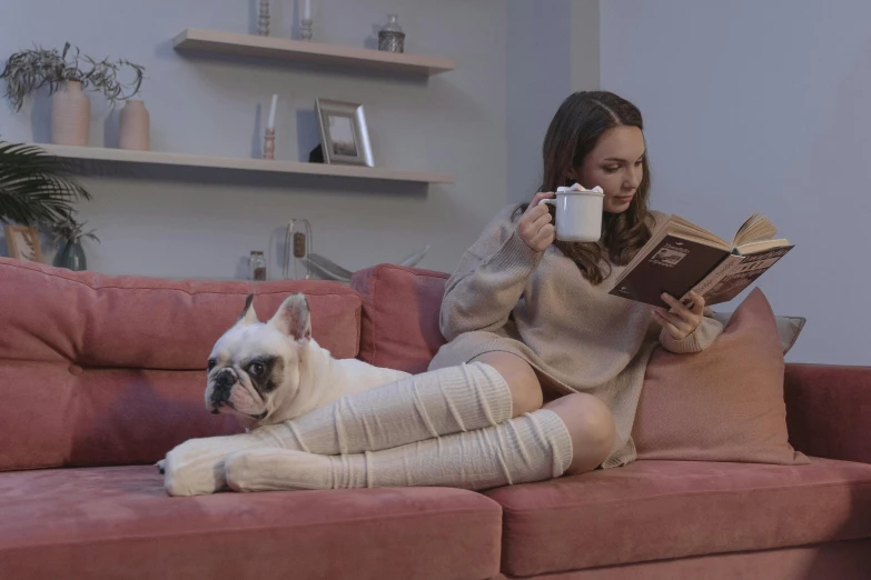 a woman sitting on a couch reading a book next to a dog, pexels contest winner, leotard and leg warmers, movie filmstill, french bulldog, bandages