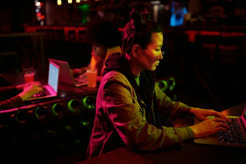 a woman sitting in front of a laptop computer, inspired by Liam Wong, happening, neon standup bar, worksafe. cinematic, people at night, profile image