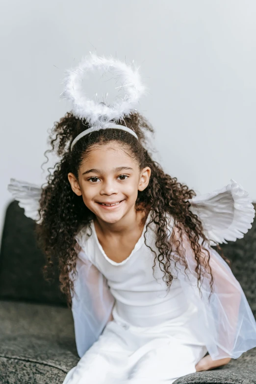 a little girl dressed as an angel sitting on a couch, inspired by Marie Angel, pexels contest winner, renaissance, mixed race, a teenage girl cheerleader, with curls, biblically acurate angel