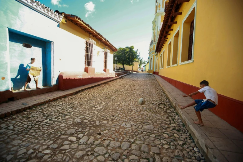 a young boy kicking a soccer ball down a cobblestone street, inspired by Ceferí Olivé, square, tourism, amanda lilleston, colonial exploration