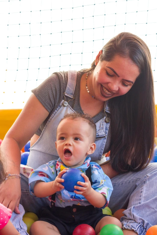 a woman and two children playing in a ball pit, wearing blue jean overalls, caio santos, babies in her lap, softplay