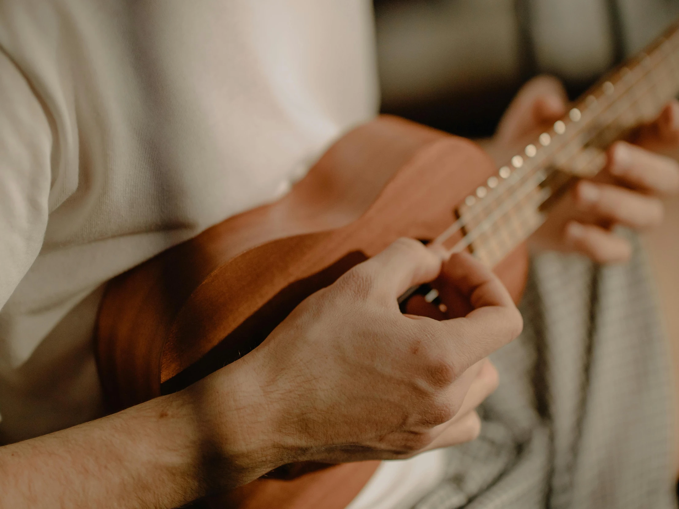 a close up of a person playing a guitar, by Emma Andijewska, pexels contest winner, ukulele, background image, warm shading, at home