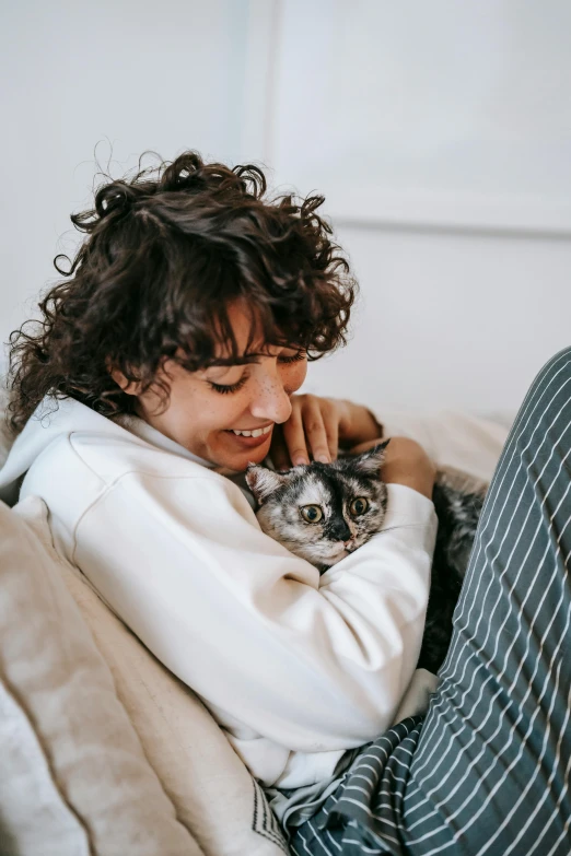 a woman sitting on a couch holding a cat, trending on pexels, curly brown hair, holding each other, gif, digital image