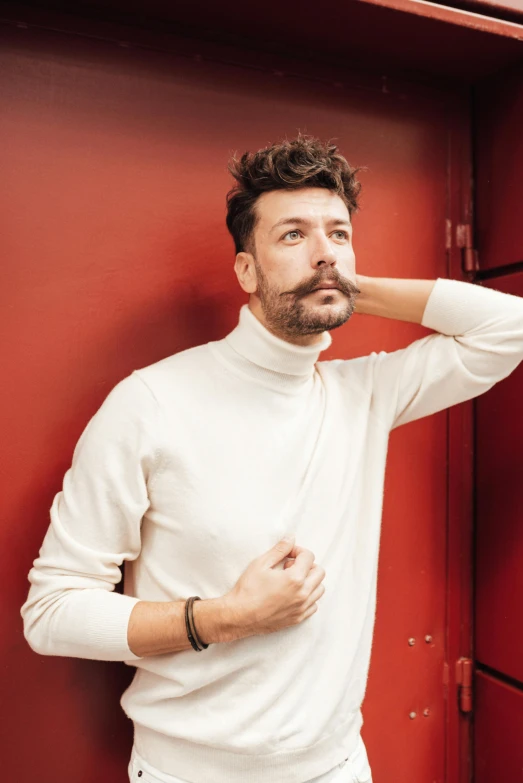 a man in a white shirt leaning against a red wall, an album cover, inspired by Germán Londoño, wearing turtleneck, demur, nicolas bouvier, promotional image