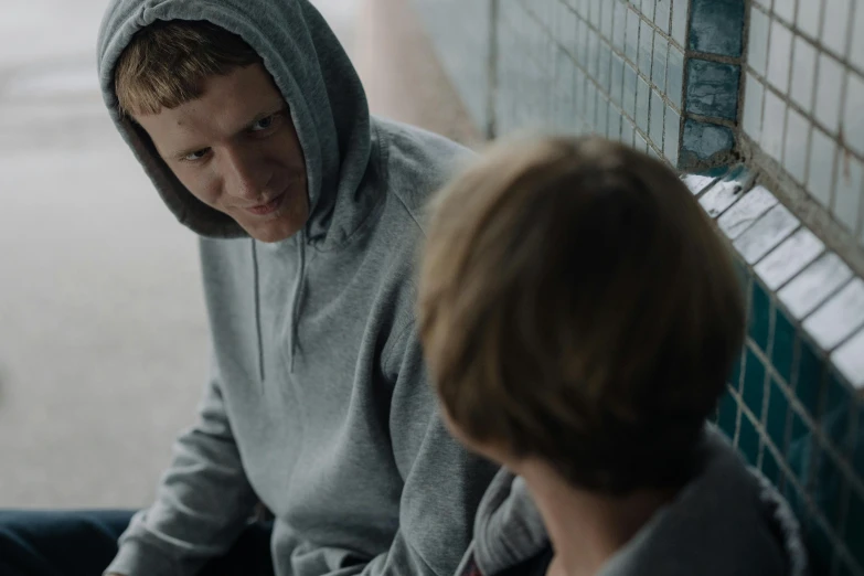 a young man sitting on a bench next to a young boy, pexels contest winner, in a hoodie, [ theatrical ], prison scene, bowater charlie and brom gerald