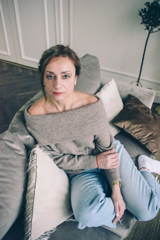 a woman sitting on a couch in a living room, a portrait, inspired by Ilka Gedő, pexels contest winner, antipodeans, low quality photo, wearing jeans, top down, épaule devant pose