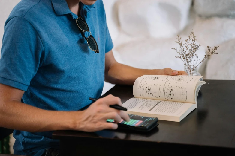 a man sitting at a table with a calculator and a book, by Carey Morris, trending on pexels, vibing to music, avatar image, taken on iphone 14 pro, casually dressed