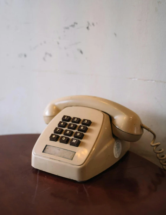 a white telephone sitting on top of a wooden table, sitting on a mocha-colored table, faded and dusty, photo from 2022, ignant