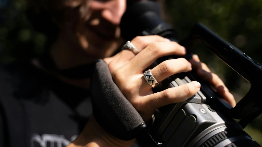 a close up of a person holding a camera, inspired by L. A. Ring, silver jewellery, dynamic angled shot, black magic crystal ring, directional sunlight skewed shot