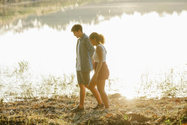 a man and a woman walking next to a body of water, happening, teenager, sun lit, romantic lead, profile image