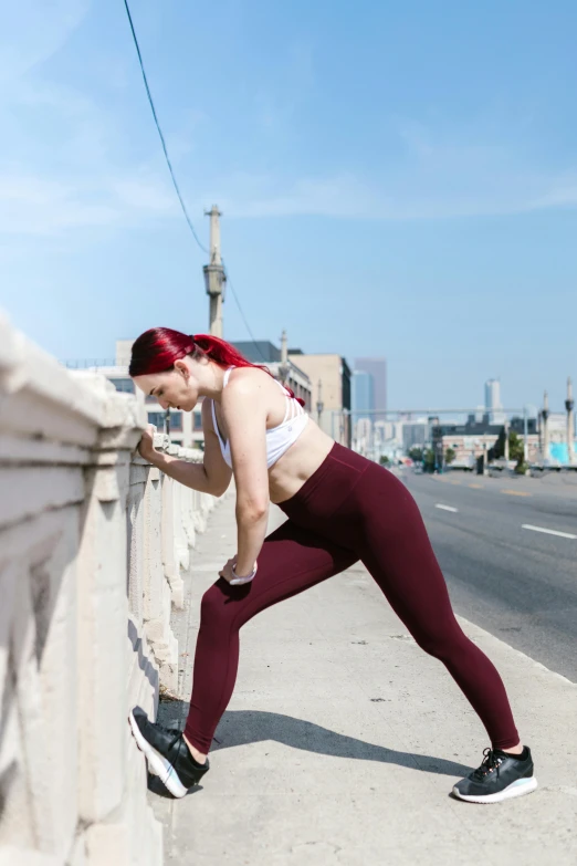 a woman stretching on the side of a bridge, maroon, curvy build, peolple run on the street, promo image