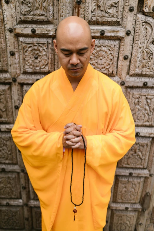 a man standing in front of a wooden door, inspired by Ma Quan, yellow robes, praying posture, connectivity, full colour