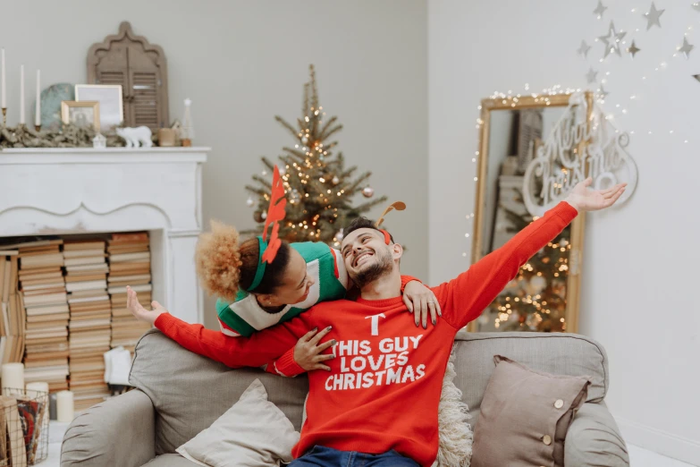 a man and woman sitting on a couch in front of a christmas tree, pexels contest winner, tachisme, wearing a sweater, celebrating, his one yes glow red, gif