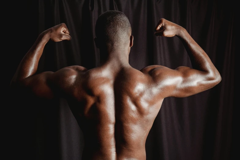 a man flexing his muscles in front of a black background, pexels contest winner, mannerism, african domme mistress, arched back, back to back, photograph taken in 2 0 2 0