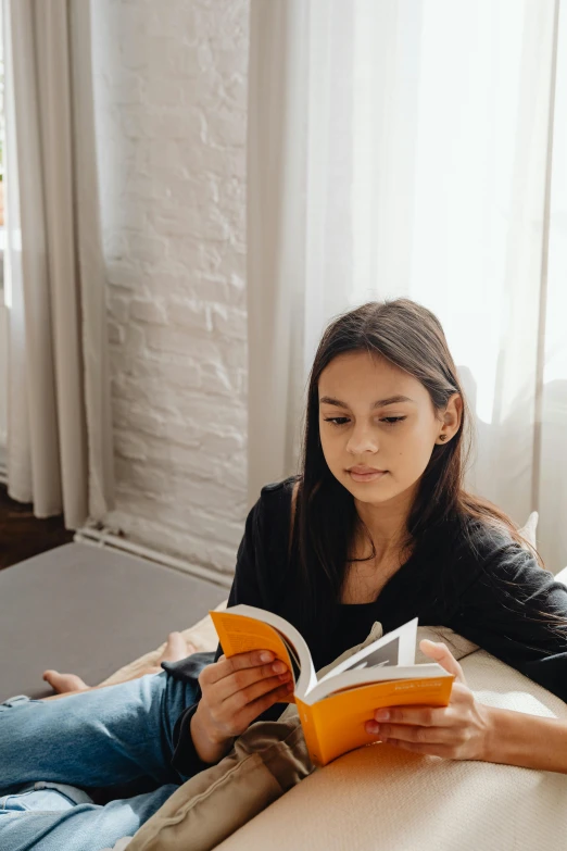 a woman sitting on a couch reading a book, by Nicolette Macnamara, pexels contest winner, portrait of teenage girl, medium shot of two characters, textbooks and books, confident looking