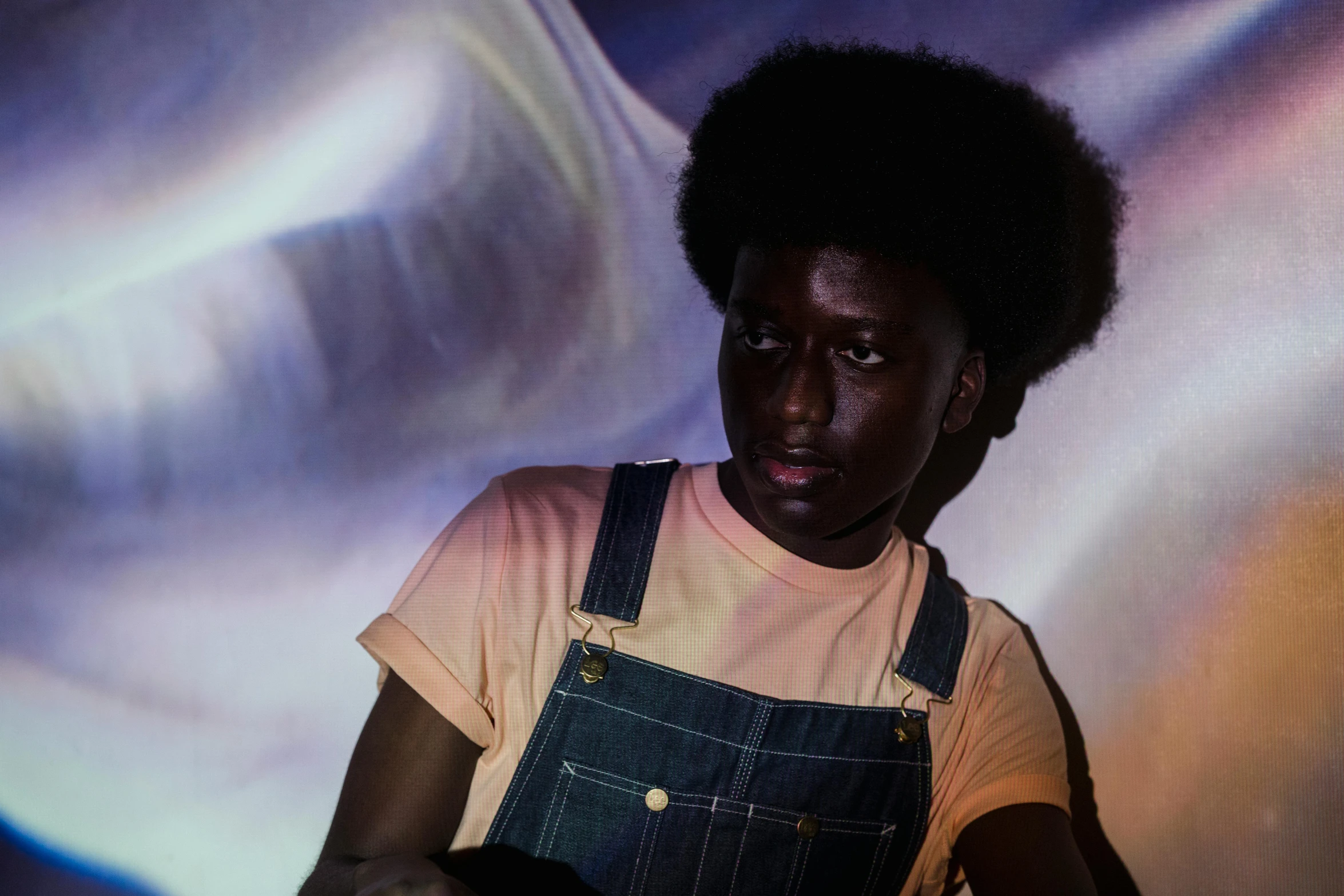 a close up of a person holding a remote control, an album cover, by Nathalie Rattner, pexels contest winner, afrofuturism, wearing blue jean overalls, black man with afro hair, light show, adut akech