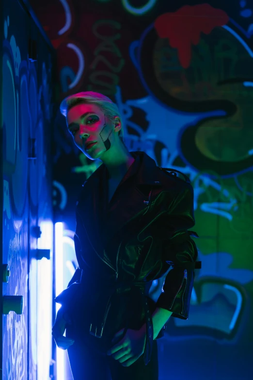 a man standing in front of a wall covered in graffiti, cyberpunk art, inspired by Elsa Bleda, trending on pexels, short blue haired woman, glowing with colored light, androgynous vampire, bella poarch